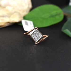 Puede incluir: Un anillo de oro rosa con un grupo cuadrado de peque&ntilde;as piedras transparentes. El anillo tiene un dise&ntilde;o &uacute;nico con una banda curva. Las piedras est&aacute;n engastadas en forma cuadrada, creando un efecto brillante. Una joya.