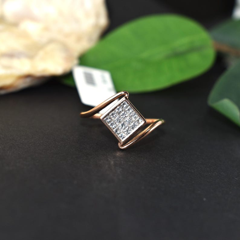 Puede incluir: Un anillo de oro rosa con un grupo cuadrado de peque&ntilde;as piedras transparentes. El anillo tiene un dise&ntilde;o &uacute;nico con una banda curva. Las piedras est&aacute;n engastadas en forma cuadrada, creando un efecto brillante. Una joya.