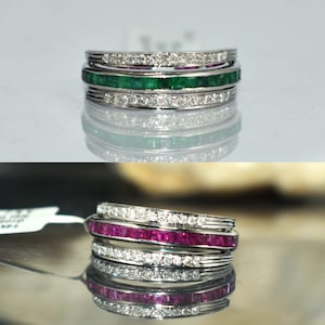 May include: Stackable rings with alternating rows of white diamonds, emeralds, and rubies. The rings are set in a silver band, creating a luxurious and elegant look. The gemstones are cut in a rectangular shape.