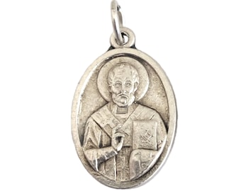 Könnte beinhalten: Ovaler Silberanhänger mit detailliertem Relief eines Heiligen mit Heiligenschein und Buch. Der Anhänger hat eine kleine Schlaufe für eine Kette. Das Design ist klassisch und religiös.