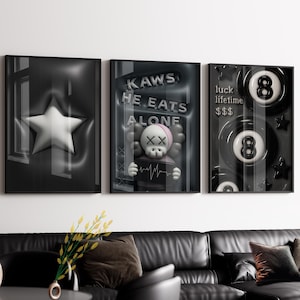 May include: Set of three framed art prints. The first features a white star on a dark background. The second displays a KAWS figure with the text "KAWS HE EATS ALONE". The third print shows two 8-ball designs with the text "luck lifetime $$$".