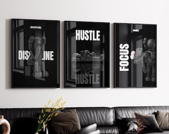 May include: Set of three black and white framed art prints. Each print features a KAWS-style figure and motivational words: "DISCIPLINE," "HUSTLE," and "FOCUS." The prints are displayed above a black leather sofa.