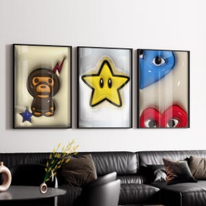 May include: Three framed wall art pieces. The first features a brown monkey-like character with a red lightning bolt and a blue star. The second is a yellow star with black eyes. The third has a blue eye and a red heart with eyes.