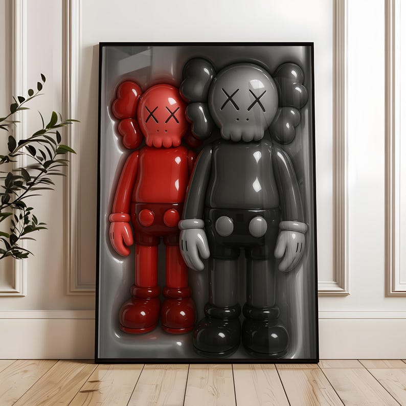 May include: Framed artwork featuring two glossy, stylized figures. One is red, the other is gray, both with distinctive skull-like faces marked with 'XX' eyes. The figures are in a molded plastic display case, set against a white wall.