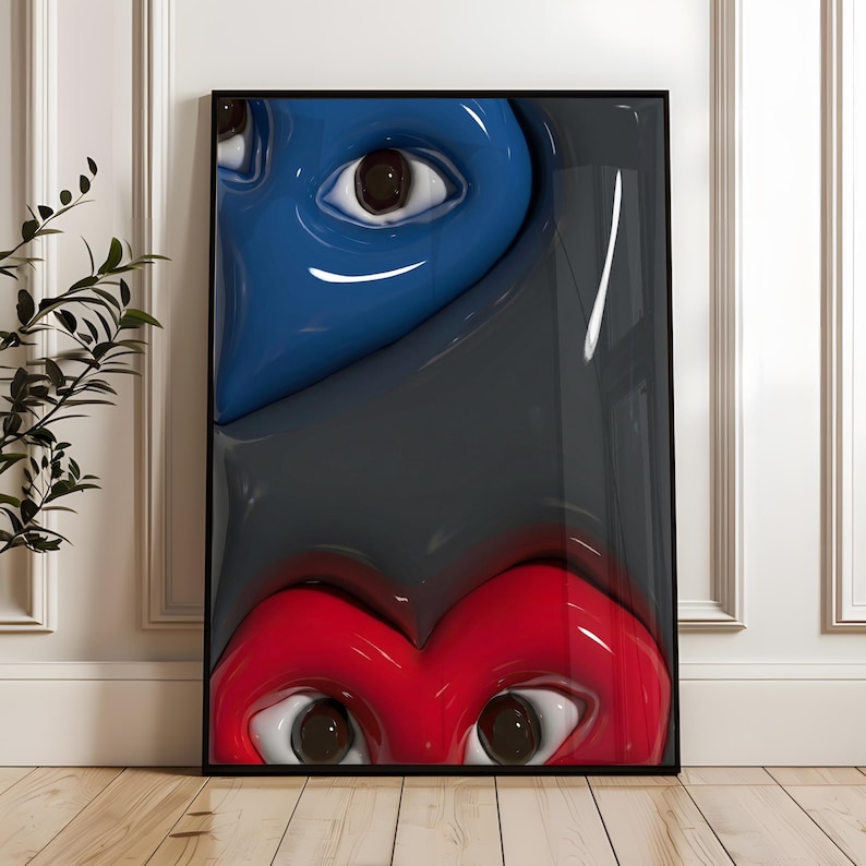 May include: Framed artwork featuring two stylized heart-shaped faces with eyes. The top face is blue, and the bottom face is red, both against a gray background. The artwork is displayed on a wooden floor.