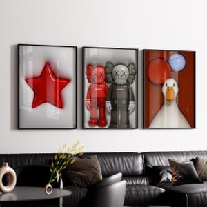 May include: Three framed art prints. The left print shows a glossy red star on a white background. The centre print features two KAWS figures. The right print depicts a white duck with red and blue balloons.