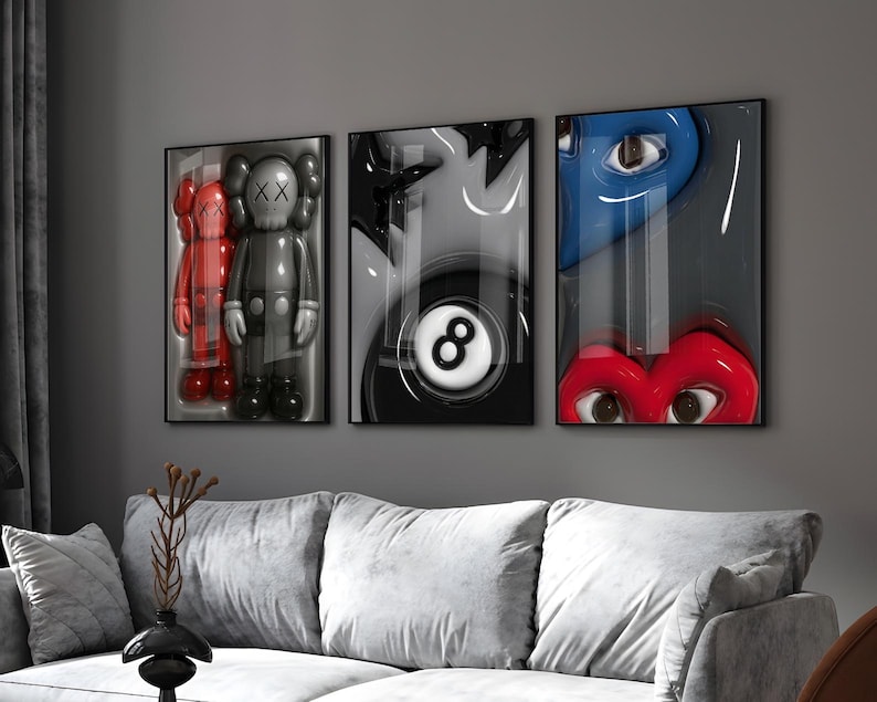 May include: Three framed art pieces with pop art themes. One features a red and gray figure, another a black and white eight ball, and the third a blue eye and red lips. The artwork is displayed above a gray sofa.