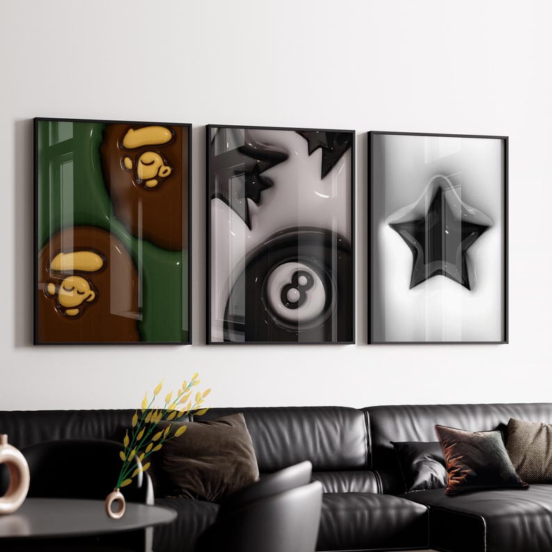 May include: Three framed art prints. The left print features a brown and green abstract design with a cartoon monkey. The centre print is a black and white image of an eight ball. The right print is a black star on a white background.