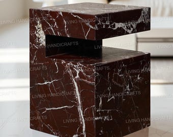 Puede incluir: Una mesa auxiliar moderna y geométrica hecha de mármol rojo oscuro con vetas blancas. La mesa tiene un diseño único y abierto con una parte superior e inferior rectangulares, y un recorte central. Esta pieza de mobiliario auxiliar añade un toque de lujo.