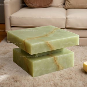 May include: A modern, two-tiered coffee table made of light green onyx. The rectangular top and base are connected by a central support. The onyx has natural brown veining, adding to its unique appearance. The table is set on a plush, light-colored rug.