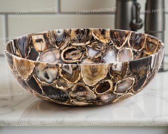 May include: A decorative, oval-shaped stone sink with a mosaic pattern of brown, beige, and white agate pieces. The sink is set on a white countertop, with a faucet and fixtures in the background. The words "LIVING HANDICRAFT" are printed on the sink.