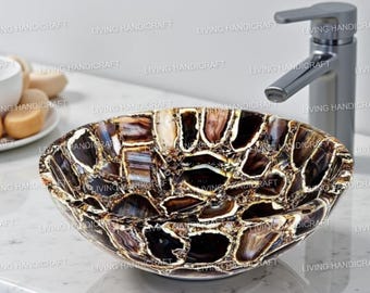 May include: A decorative, oval-shaped bathroom sink made of polished stone. The sink features a mosaic pattern of brown, black, and cream-colored pieces. A chrome faucet is visible in the background. The words "LIVING HANDICRAFT" are printed on the image.