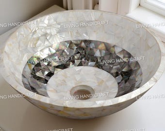 May include: A round, decorative sink with a mosaic design. The sink features a white and iridescent mother-of-pearl pattern, with a dark gray and white center. The sink has a central drain hole.
