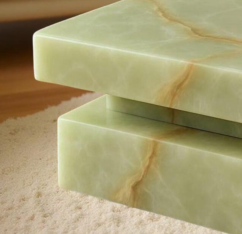 May include: Close-up of a two-tiered, rectangular table with a light green onyx surface. The onyx has natural brown veining, creating a unique pattern. The table is set on a light-colored, textured rug.