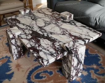 Op de afbeelding: Een rechthoekige salontafel van wit marmer met donkerpaarse adering. De tafel heeft een uniek ontwerp met geometrische poten en steunen. De marmeren tafel is een statement piece voor een woonkamer.
