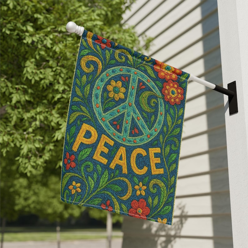 May include: A decorative outdoor flag featuring a peace sign and the word "PEACE" in yellow. The flag has a blue background with floral and leaf patterns in green, orange, and yellow. The flag is mounted on a white pole.