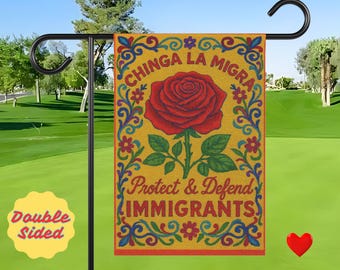 Puede incluir: Una bandera de jardín de doble cara con una rosa roja y el texto "Chinga La Migra" y "Protect & Defend IMMIGRANTS" sobre un fondo amarillo. La bandera se muestra en un soporte de metal negro sobre un césped verde.