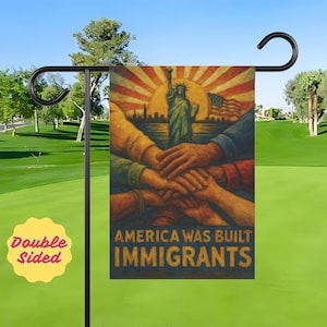 Puede incluir: Bandera de jardín de doble cara con un diseño patriótico. La bandera presenta la Estatua de la Libertad, un sol naciente y la bandera estadounidense. El texto dice "AMERICA WAS BUILT BY IMMIGRANTS". La bandera se muestra en un soporte de metal negro.