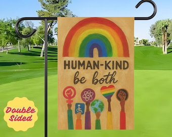 May include: A double-sided garden flag with a rainbow and the words "HUMAN-KIND be both." The flag features various symbols of inclusivity, including a fist, a heart, and a globe. The flag is displayed on a black metal stand.