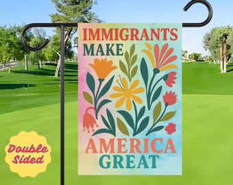 Puede incluir: Una bandera de jardín de doble cara con el texto "IMMIGRANTS MAKE AMERICA GREAT" en rojo y turquesa. La bandera presenta ilustraciones florales coloridas en naranja, amarillo y rojo sobre un fondo de acuarela. La bandera se muestra en un soporte de metal negro.