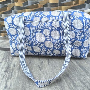 Könnte beinhalten: Blau-weiß gemusterte Tragetasche mit passenden Griffen. Die Tasche hat ein großes Blumenmuster und eine kleine Tasche auf der Vorderseite. Die Griffe sind hellblau mit einem Streifenmuster.