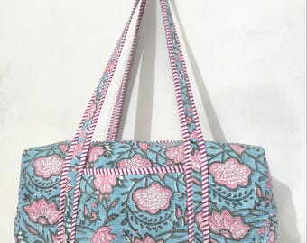 May include: A rectangular tote bag with a floral pattern in pink and gray on a light blue background. The bag has two long pink and white striped handles and a matching trim. The bag has a pocket on the front.