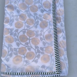 May include: White fabric with a floral pattern in shades of tan and gray. The fabric has a border of black and green stripes. The floral design features large, stylized flowers and winding vines.