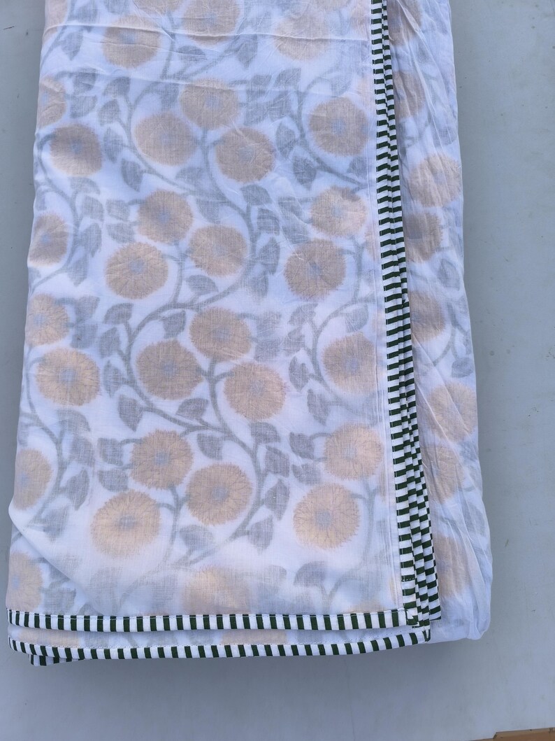 May include: White fabric with a floral pattern in shades of tan and gray. The fabric has a border of black and green stripes. The floral design features large, stylized flowers and winding vines.
