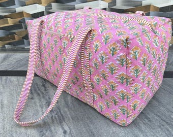 May include: A pink tote bag with a floral pattern in yellow and green. The bag has two handles with a striped design in pink and white. The bag is made of a quilted fabric.