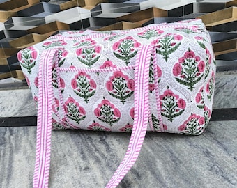 May include: A white tote bag with a pink floral pattern and pink striped handles. The bag features a repeating design of pink flowers and green leaves. The bag is made of a soft, quilted fabric.
