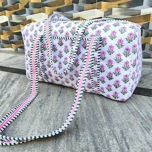 Puede incluir: Bolsa de viaje blanca con un estampado floral rosa y verde. La bolsa tiene asas a juego a rayas en blanco, rosa y verde. La bolsa rectangular es de tela.