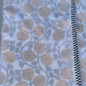 May include: White fabric with a repeating pattern of large, yellow-tan flowers and gray leaves on vines. A border of black and white vertical stripes runs along one edge. The fabric is folded, showing the pattern and border.
