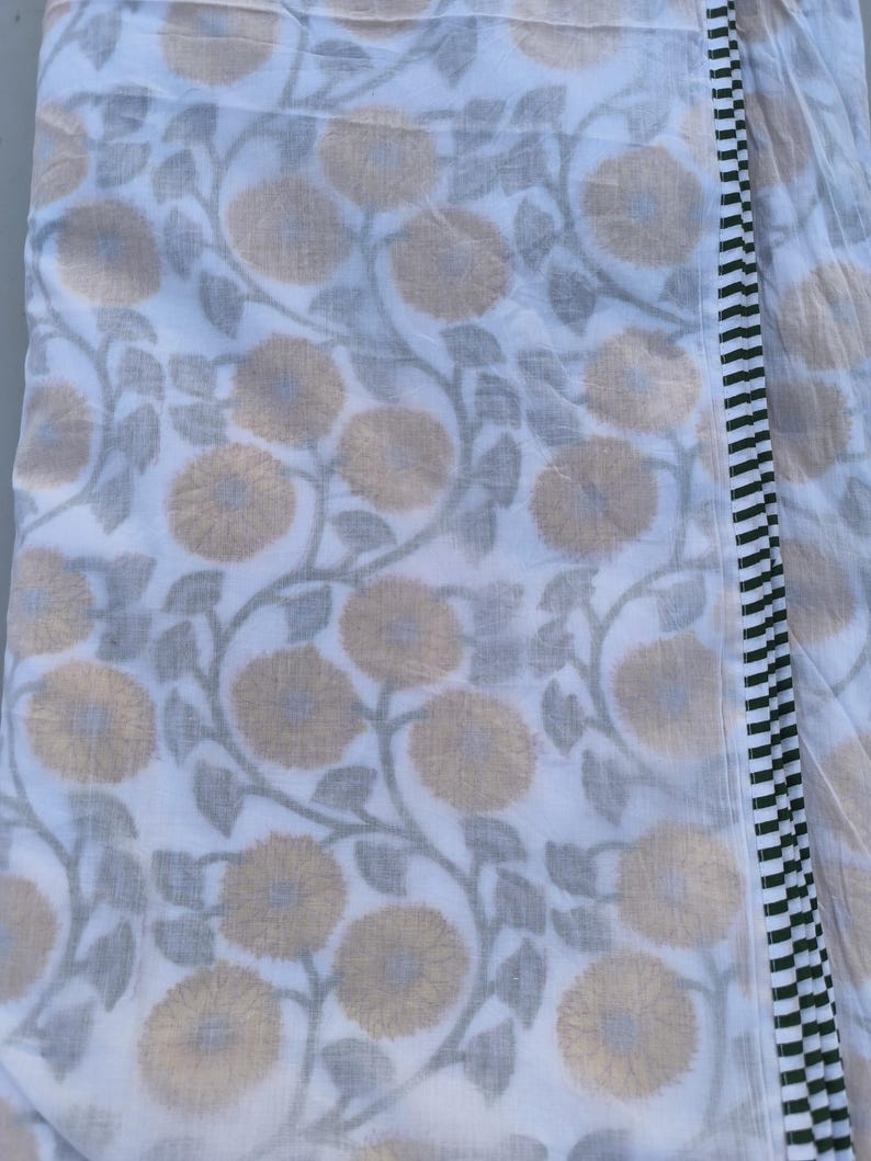 May include: White fabric with a repeating pattern of large, yellow-tan flowers and gray leaves on vines. A border of black and white vertical stripes runs along one edge. The fabric is folded, showing the pattern and border.