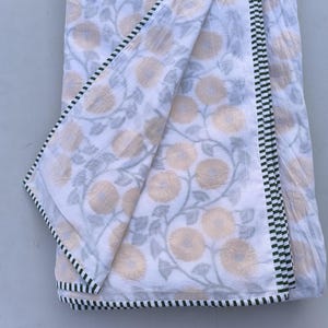 May include: White fabric with a floral pattern in shades of yellow and gray. The fabric has a black and white checkered border. The floral design features large, stylized flowers and winding vines, creating a soft, natural aesthetic.