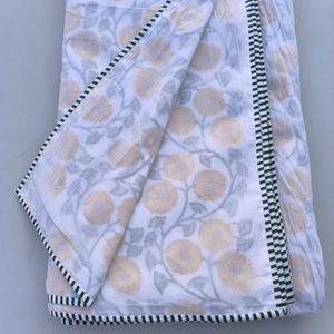 May include: White floral patterned fabric with a green and black checkered border. The fabric features a repeating pattern of yellow flowers and gray leaves. The fabric is folded, showing the pattern and border details.