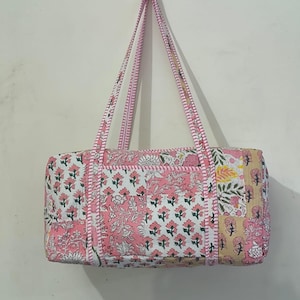 Puede incluir: Bolso tote rectangular con estampados florales rosas sobre fondo blanco. El bolso tiene asas y ribetes rosas. El diseño incluye un patchwork de estampados florales y un borde rosa liso. El bolso está colgado contra una pared blanca.