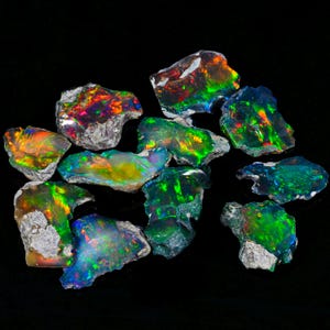 Peut inclure: Plusieurs pierres d'opale brutes, présentant des couleurs vives comme le vert, l'orange, le rouge et le bleu. Les opales ont un aspect naturel et brut avec une surface texturée, sur fond noir.