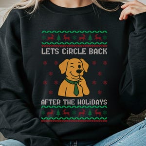 May include: Black sweatshirt with a festive design. The design includes the text "Lets Circle Back After The Holidays" above and below a cartoon dog wearing a green tie. The top and bottom of the design have a repeating pattern of reindeer and Christmas trees.