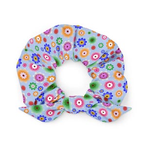 May include: A light blue scrunchie with a colorful floral pattern. The flowers are in shades of pink, orange, yellow, green, and blue. The scrunchie is tied in a bow.