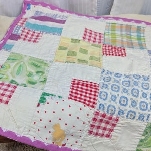 May include: A patchwork quilt with a variety of colorful fabrics, including red, green, blue, and yellow. The quilt is edged with a purple trim and is displayed on a small bed.