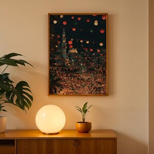 May include: A framed art print depicts a nighttime cityscape with a mosque and string lights. A round, glowing lamp sits on a wooden cabinet, with a potted plant to the left and a small plant in a terracotta pot to the right.