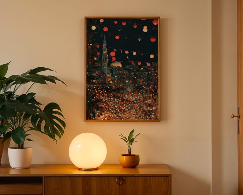 May include: A framed art print depicts a nighttime cityscape with a mosque and string lights. A round, glowing lamp sits on a wooden cabinet, with a potted plant to the left and a small plant in a terracotta pot to the right.