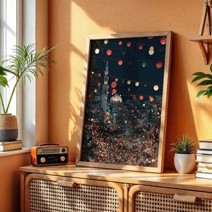 May include: A framed art print depicting a nighttime cityscape with string lights. The artwork is in a wooden frame and leans against a wall. A small orange radio sits on a wooden cabinet. Potted plants and books are also visible.