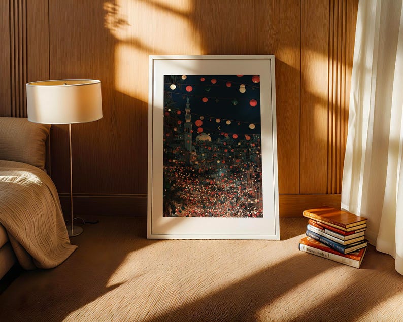May include: A framed art print with a white border, depicting a colorful cityscape at night, leans against a wooden wall. A stack of books and a floor lamp with a beige shade are nearby. The room has a warm, inviting atmosphere.