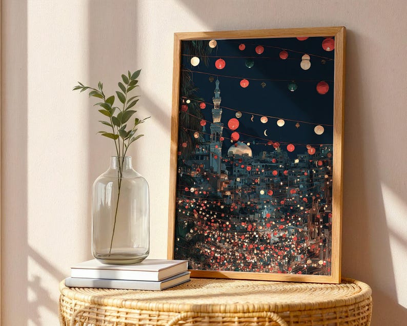 May include: A framed art print depicting a nighttime cityscape with a mosque and string lights. The artwork features a warm color palette with red, white, and green accents. A clear glass vase with greenery and a stack of books sit in front of the artwork.