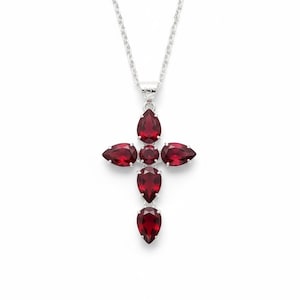 May include: A silver pendant necklace with a cross design. The cross is embellished with multiple teardrop-shaped, deep red gemstones. The necklace hangs from a delicate silver chain, creating a striking contrast against the white background.