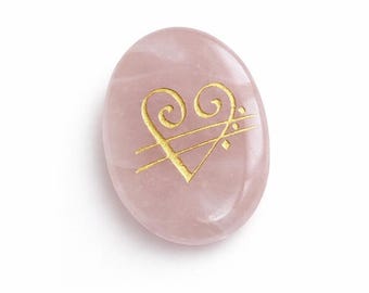Peut inclure: Une pierre de quartz rose ovale et lisse, ornée d'un motif de cœur doré. La pierre rose présente une surface polie, et le cœur doré est gravé dans la pierre. Le motif est centré sur la pierre.