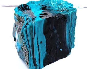 Könnte beinhalten: Ein Steinblock mit rauer, strukturierter Oberfläche, bemalt mit einer auffälligen Kombination aus Türkis und Schwarz. Die Farben sind geschichtet und gewirbelt, wodurch ein Marmoreffekt entsteht. Der Stein ist ein einzigartiger Dekorationsartikel.