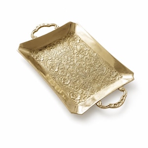 Puede incluir: Una bandeja rectangular dorada con intrincados diseños florales y de hojas. La bandeja tiene dos asas curvas y un borde elevado. La superficie está cubierta con un diseño en relieve detallado. La bandeja es de metal y tiene un acabado brillante.