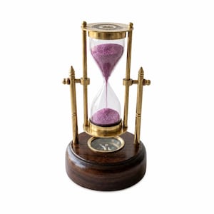 May include: An hourglass with a brass frame and a wooden base. The glass chamber contains purple sand. A compass is set into the wooden base. The hourglass is a decorative item.